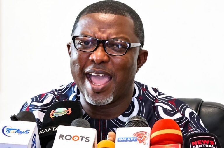 A man speaking at a press conference with multiple microphones.
