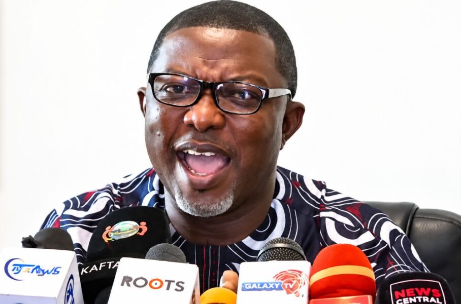 A man speaking at a press conference with multiple microphones.