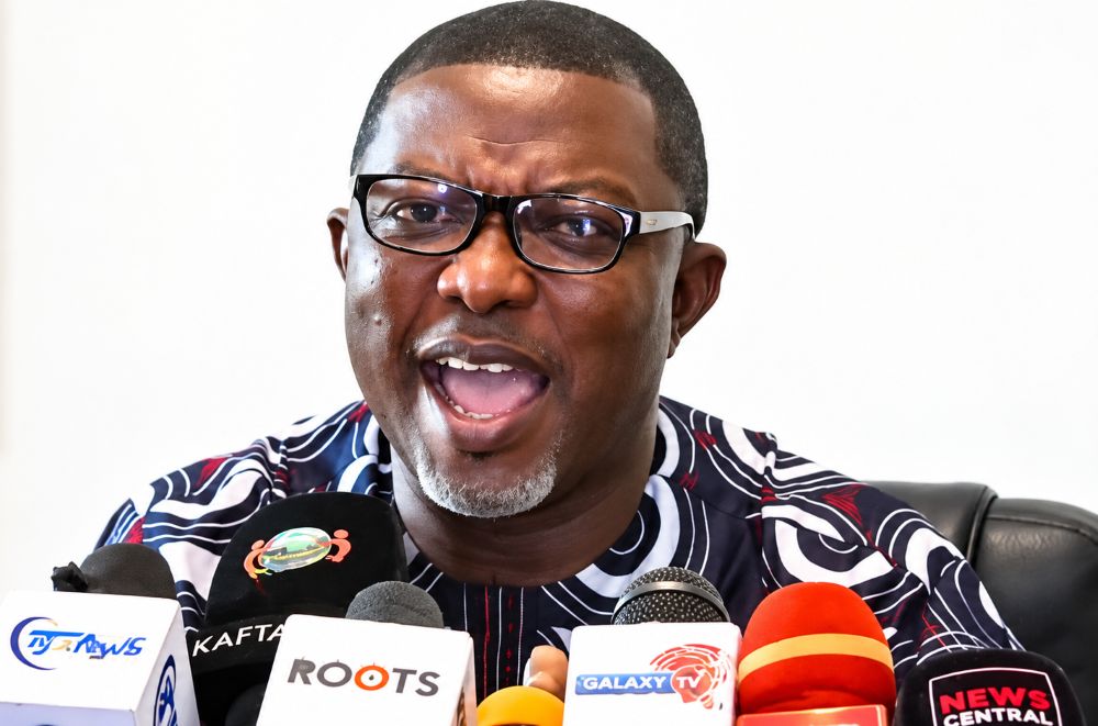 A man speaking at a press conference with multiple microphones.