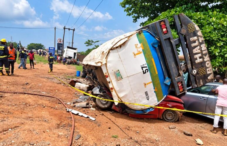 Overturned fuel tanker truck crushed a red car on road.