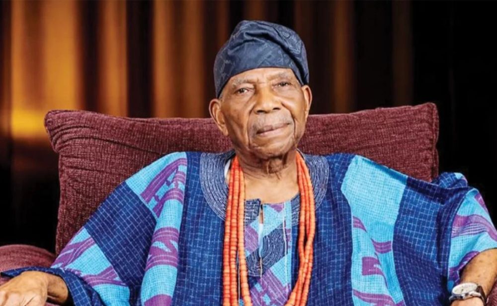 Distinguished man in traditional blue Yoruba attire and coral beads.